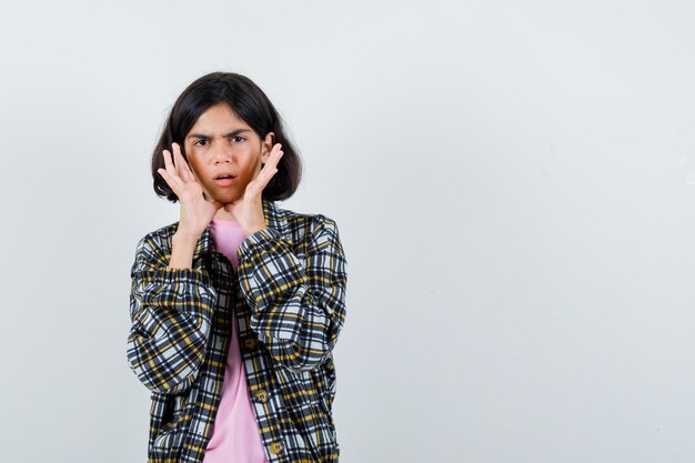 Young girl holding hands near mouth as calling someone in checked shirt and pink t-shirt and looking serious