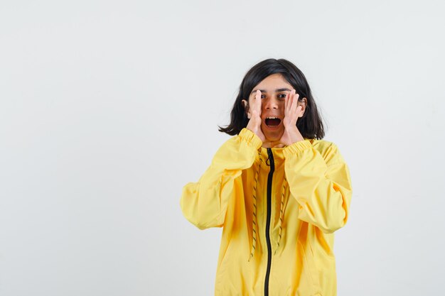 Young girl holding hands near mouth, calling someone in yellow bomber jacket and looking pretty