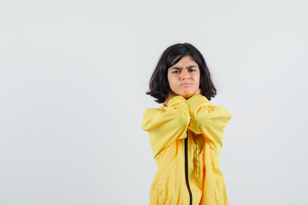 Молодая девушка держит руки на шее в желтой куртке-бомбардировщике и выглядит серьезно