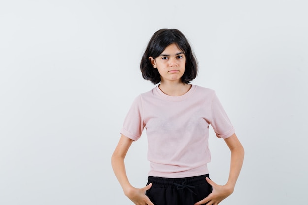 Young girl holding hands on waist in pink t-shirt and black pants and looking cute