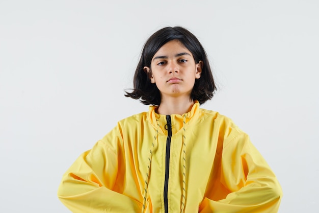 Young girl holding hands on waist in yellow bomber jacket and looking serious