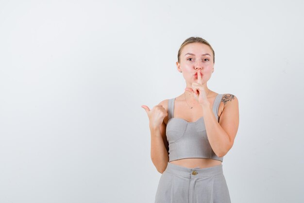 Young girl holding her finger on her mouth and showing the back with her thumb on white background