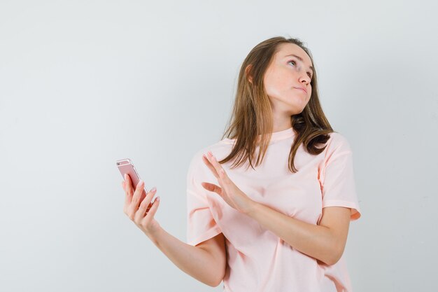 Young girl holding mobile phone in pink t-shirt and looking irritated , front view.