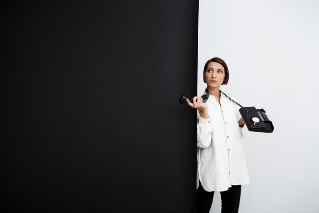 Young girl holding old phone over black and white wall