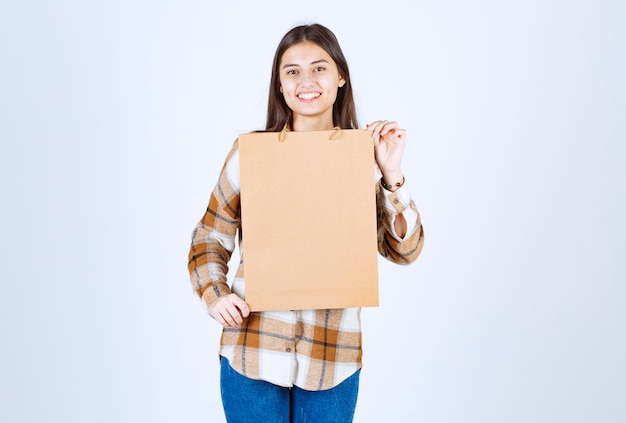 Young girl holding paper craft package and standing over white wall. 
