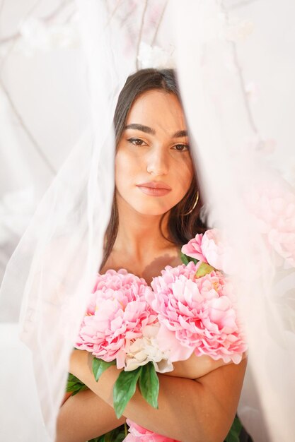 Young girl holding pink flowers under the tulle High quality photo