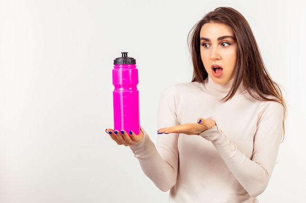 Молодая девушка держит розовую бутылку с водой, указывая на нее рукой