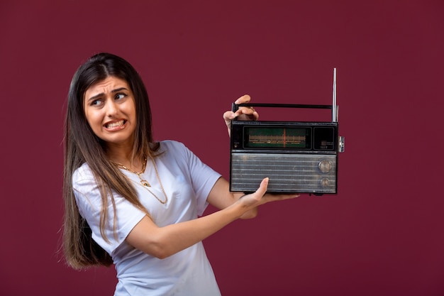 Giovane ragazza con in mano una radio vintage e disturbata dal volume.