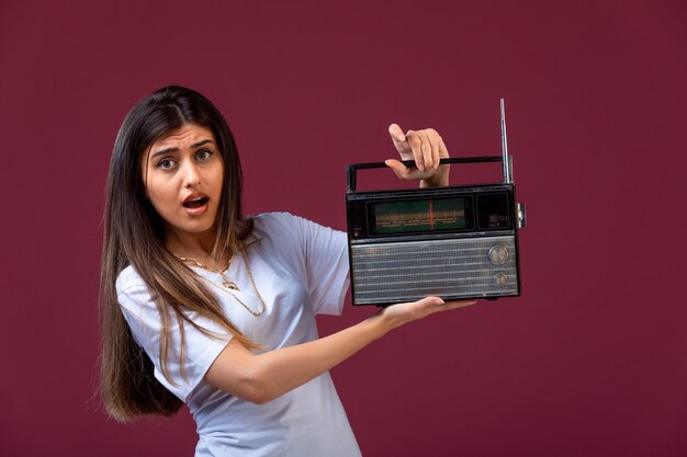 Young girl holding a vintage radio in hand and looks surprised