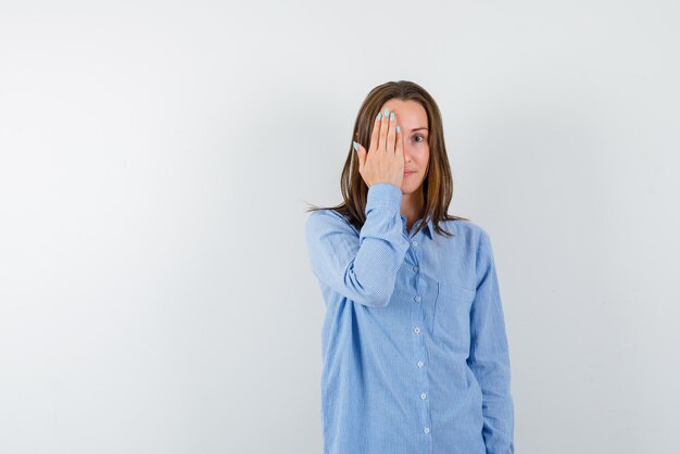 A young girl holds one eye with her hand