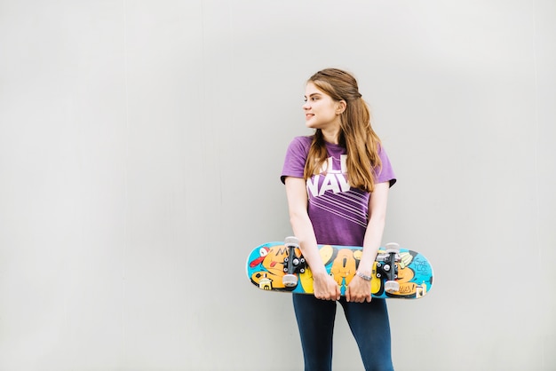 Young girl holds skateboard while looking to the right