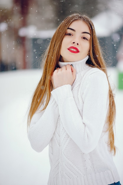 Бесплатное фото Молодая девушка в белом свитере стоит в зимнем парке