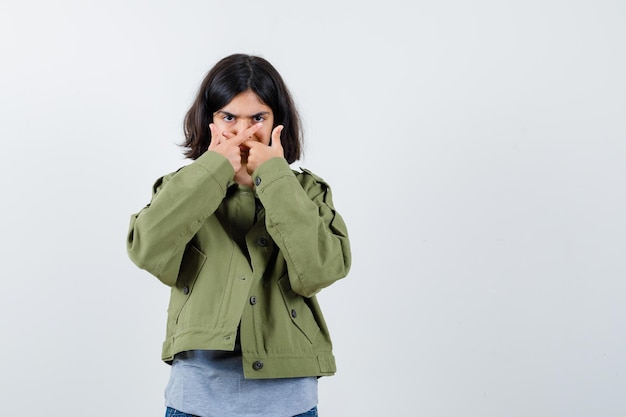 Бесплатное фото Молодая девушка в сером свитере, куртке цвета хаки, джинсовых штанах, скрестив две руки, не жестикулирующая и серьезная, вид спереди.