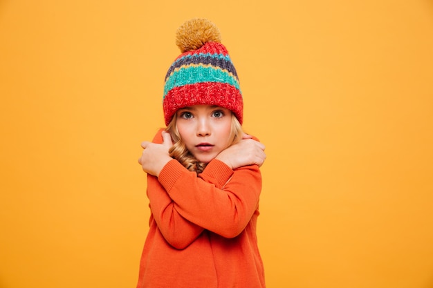 Бесплатное фото Молодая девушка в свитере и шляпе с холодной и глядя на камеру над апельсином