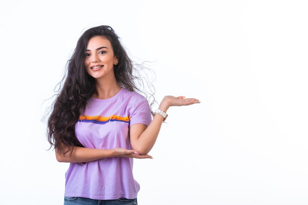 Young girl introducing something with hand on white wall and smiling.