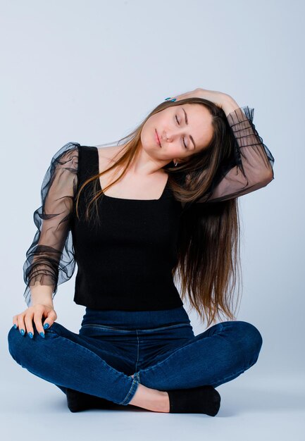 Young girl is calming down by putting hand on heand and sitting on floor on white background