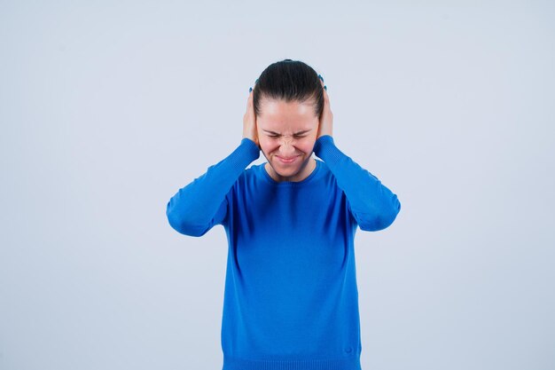 Young girl is covering her ears with hands on white background