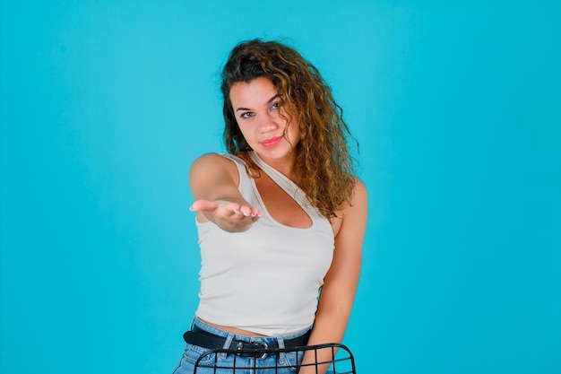 Young girl is extending her handful to camera on blue background