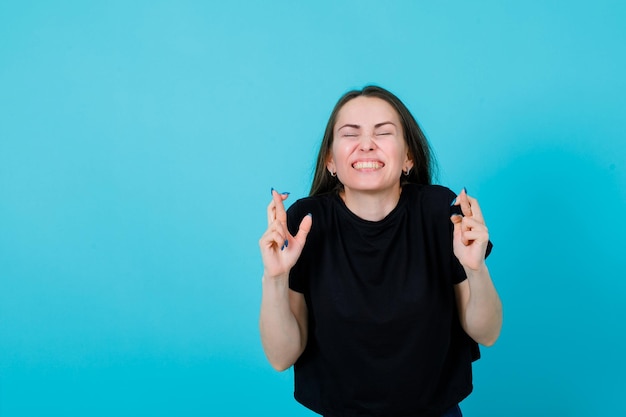 Young girl is feeling happy by raising up her crossed fingers on blue background