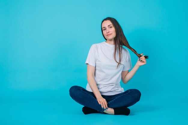 Young girl is holding har by sitting on floor on blue background