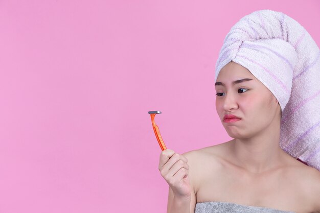 Young girl is holding shaver and feeling bored in the rest roon on pink wall.