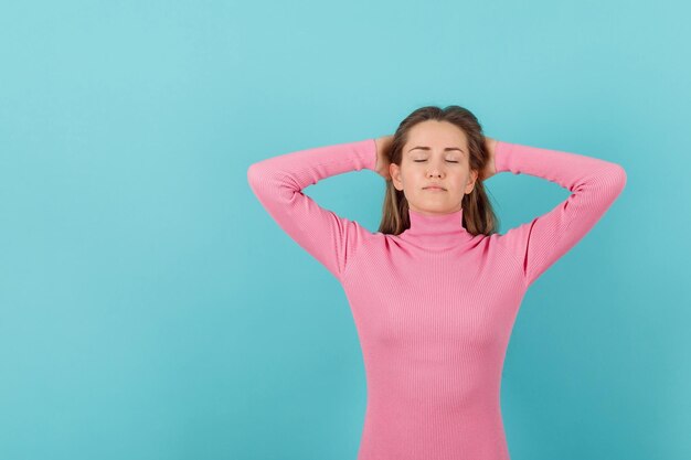 Young girl is imagining by holding hands behind head on blue background