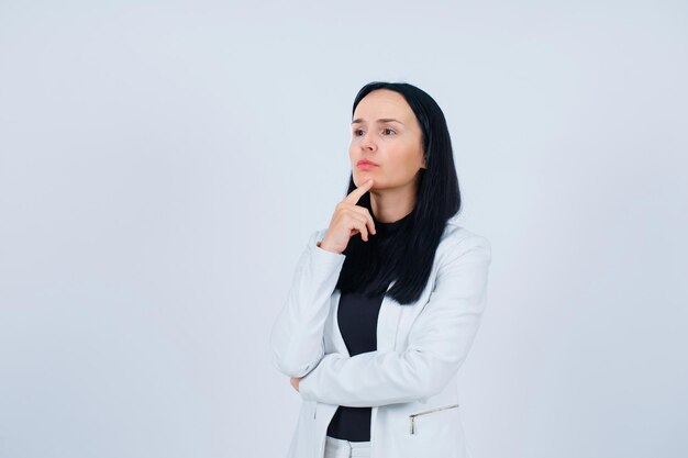 Young girl is looking away by holding forefinger on chin on white background