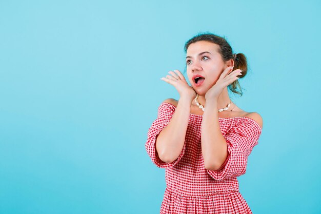 Young girl is looking away by holding hands on cheeks on blue background