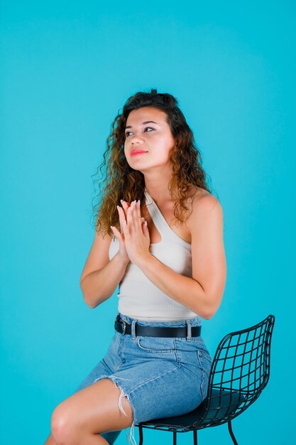 Young girl is looking away by holding hands together on chest on blue background