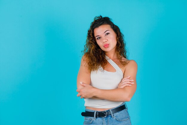 Young girl is looking at camera by crossing arms on blue background