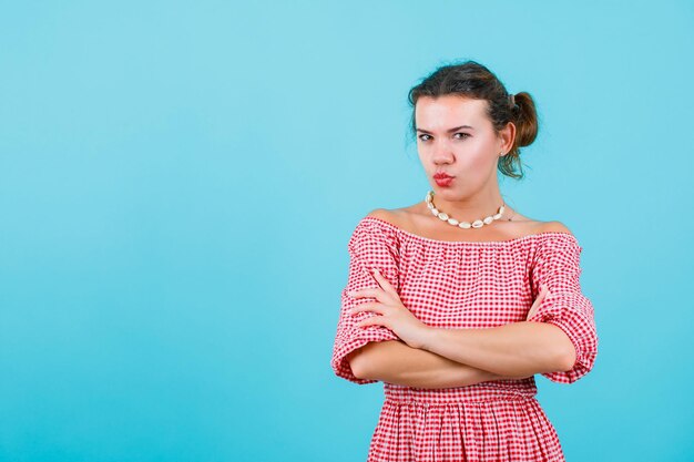 Young girl is looking at camera by crossing arms on blue background