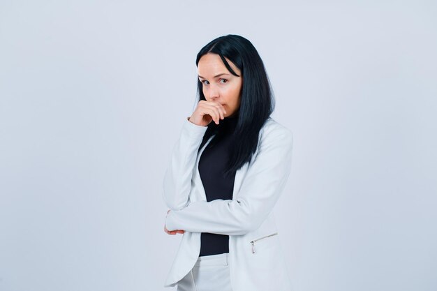 Young girl is looking at camera by holding hand on mouth on white background