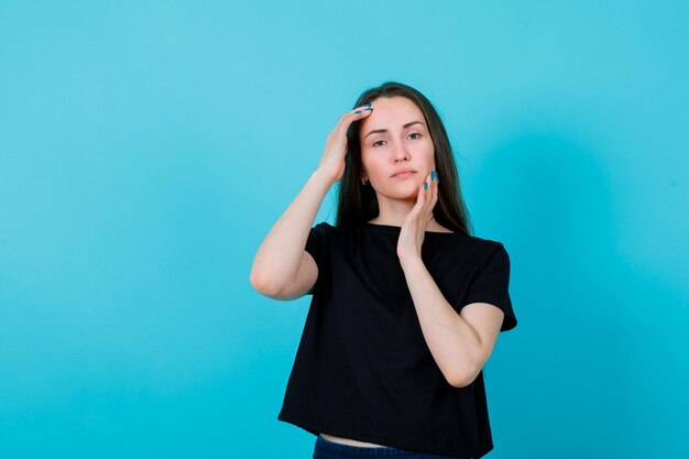 Young girl is looking at camera by holding hands around face on blue background