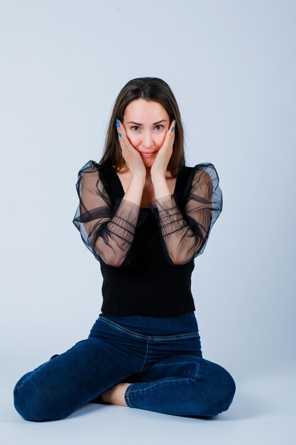 Young girl is looking at camera by holding hands on cheeks on white background