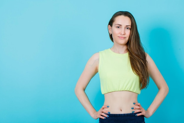 Young girl is looking at camera by putting hands on waist on blue background