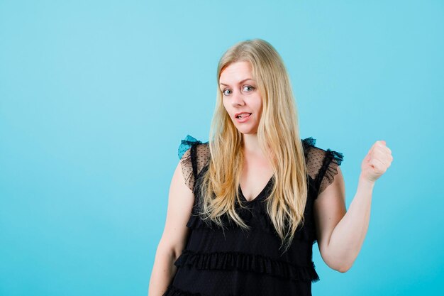 Young girl is looking at camera by raising up her fist on blue background