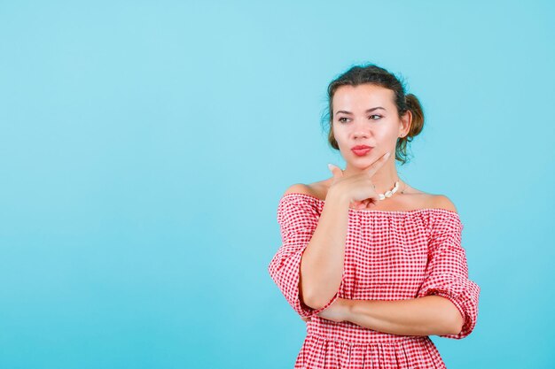 Young girl is looking down by holding forefinger on chin on blue background