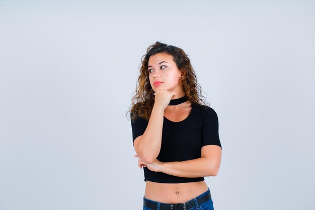 Young girl is looking left by putting hand on chin on white background