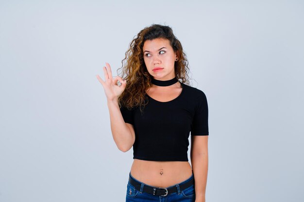 Young girl is looking left by showing okay gesture on white background