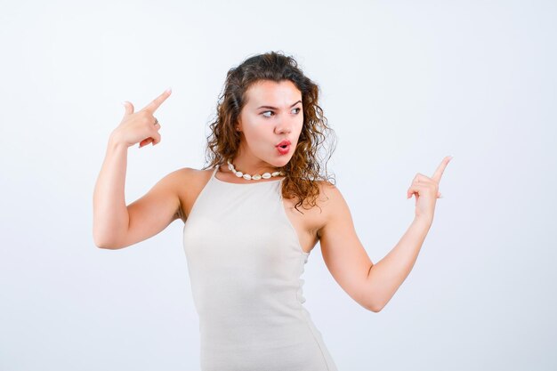 Young girl is looking right by pointing up with forefingers on white background