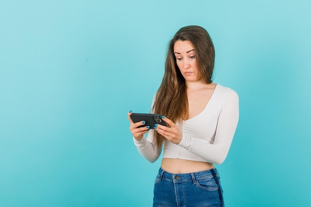 Young girl is looking at smartphone screen in surprise on blue background