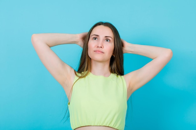 Free photo young girl is looking up by holding hands behind head on blue background