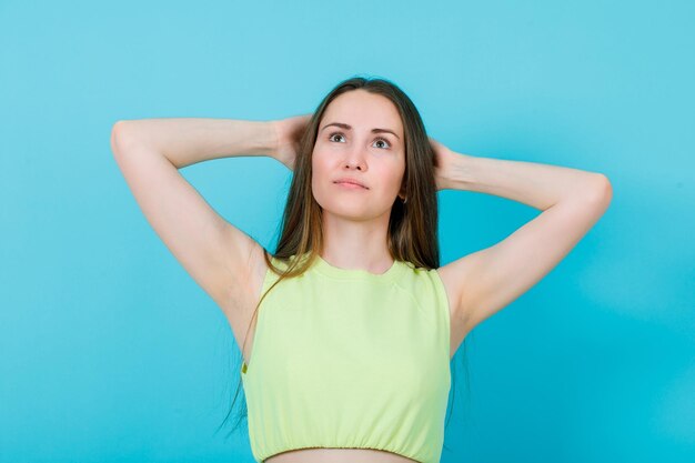 Young girl is looking up by holding hands behind head on blue background