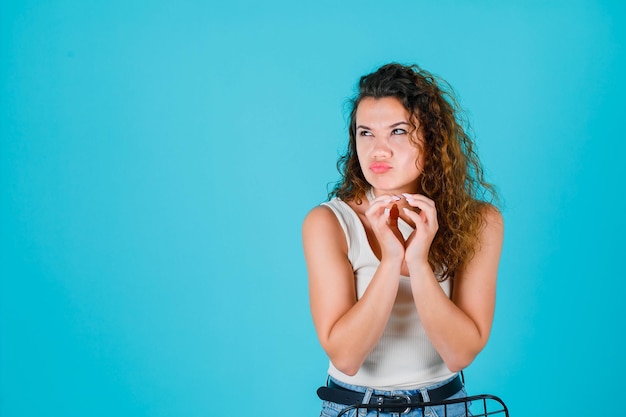 Young girl is looking up by holding hands together on chest on blue background