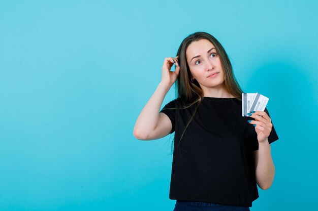 Молодая девушка смотрит вверх и держит кредитные карты на синем фоне