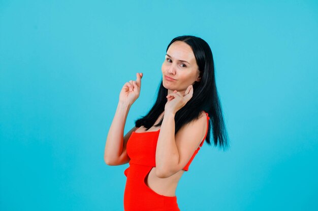 Young girl is raising up her hands and crossing fingers on blue background