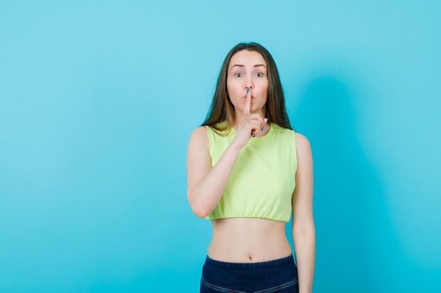 Foto gratuita la ragazza sta mostrando il gesto del silenzio tenendo l'indice sulle labbra su sfondo blu