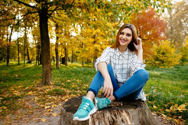 Young girl is sitting on a stump in the autumn park.
