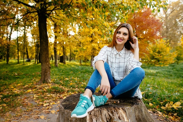 Молодая девушка сидит на пне в осеннем парке.