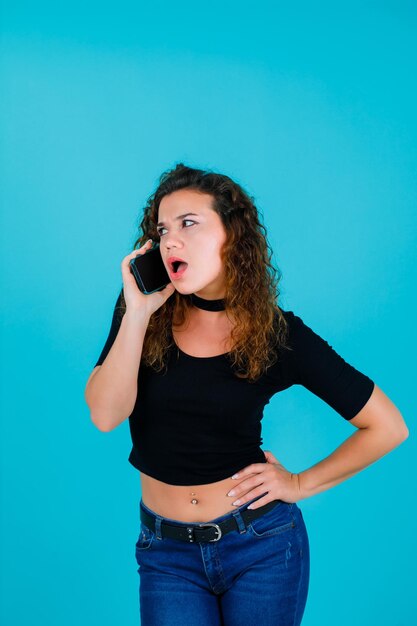 Young girl is talking on phone by putting hand on waist on blue background